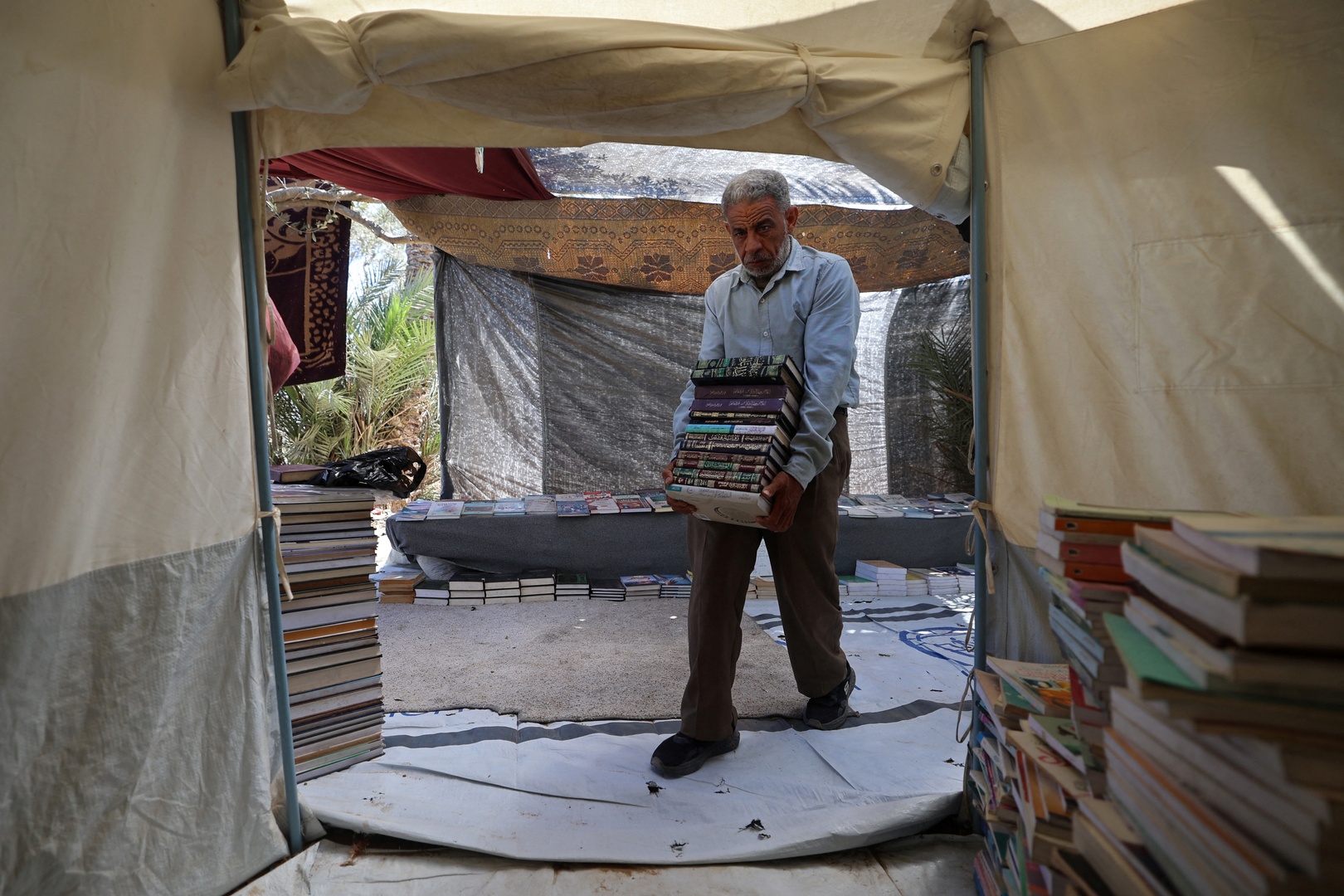 Mohammed Saad, a displaced Palestinian bookseller carries books while arranging them for customers at his mobile bookstore, in order to sell and lend the books to readers along the roadside in Deir el-Balah, central Gaza Strip on July 2, 2026. [Eyad Baba/AFP]