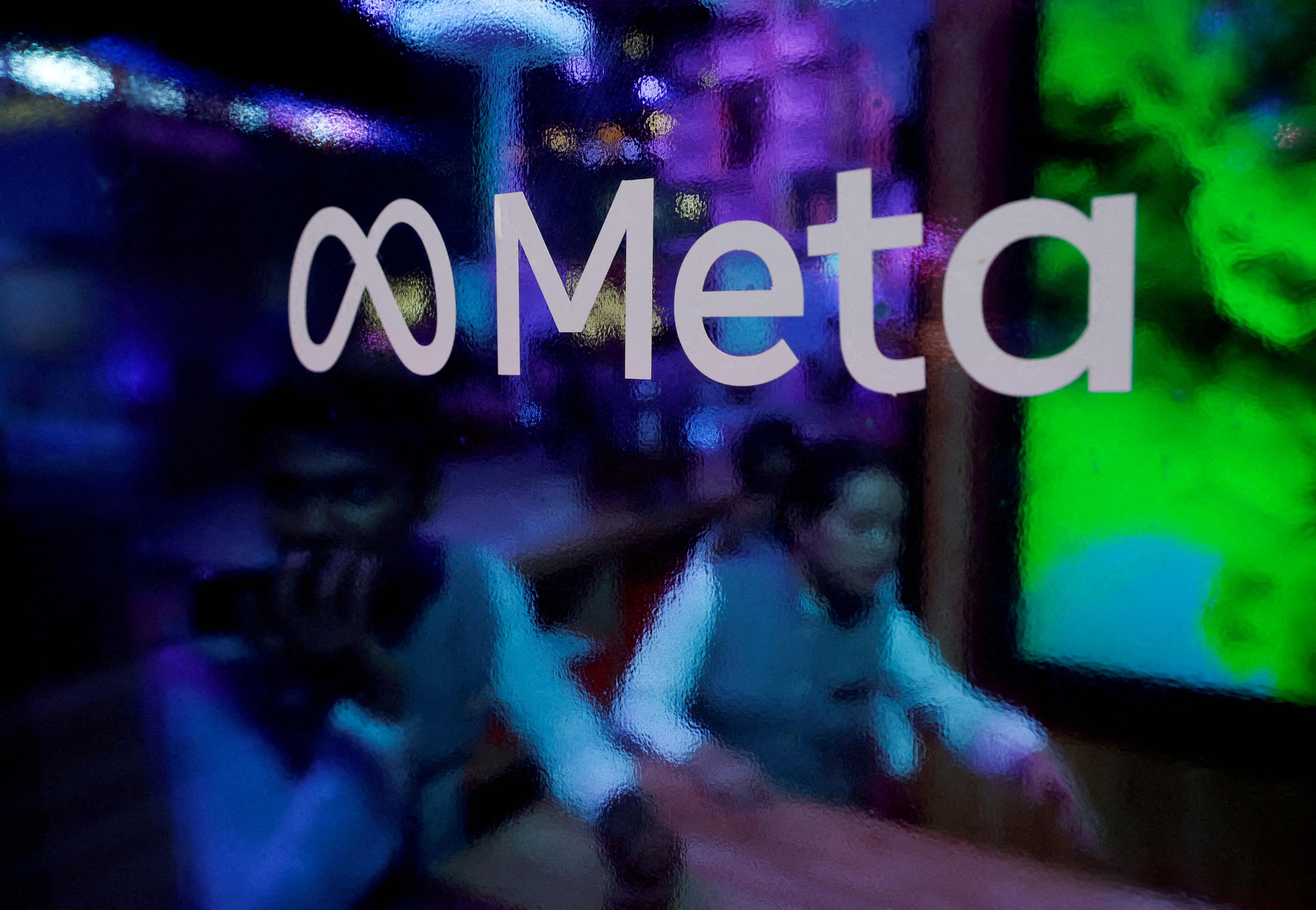 People are seen behind a logo of Meta Platforms, during a conference in Mumbai, India