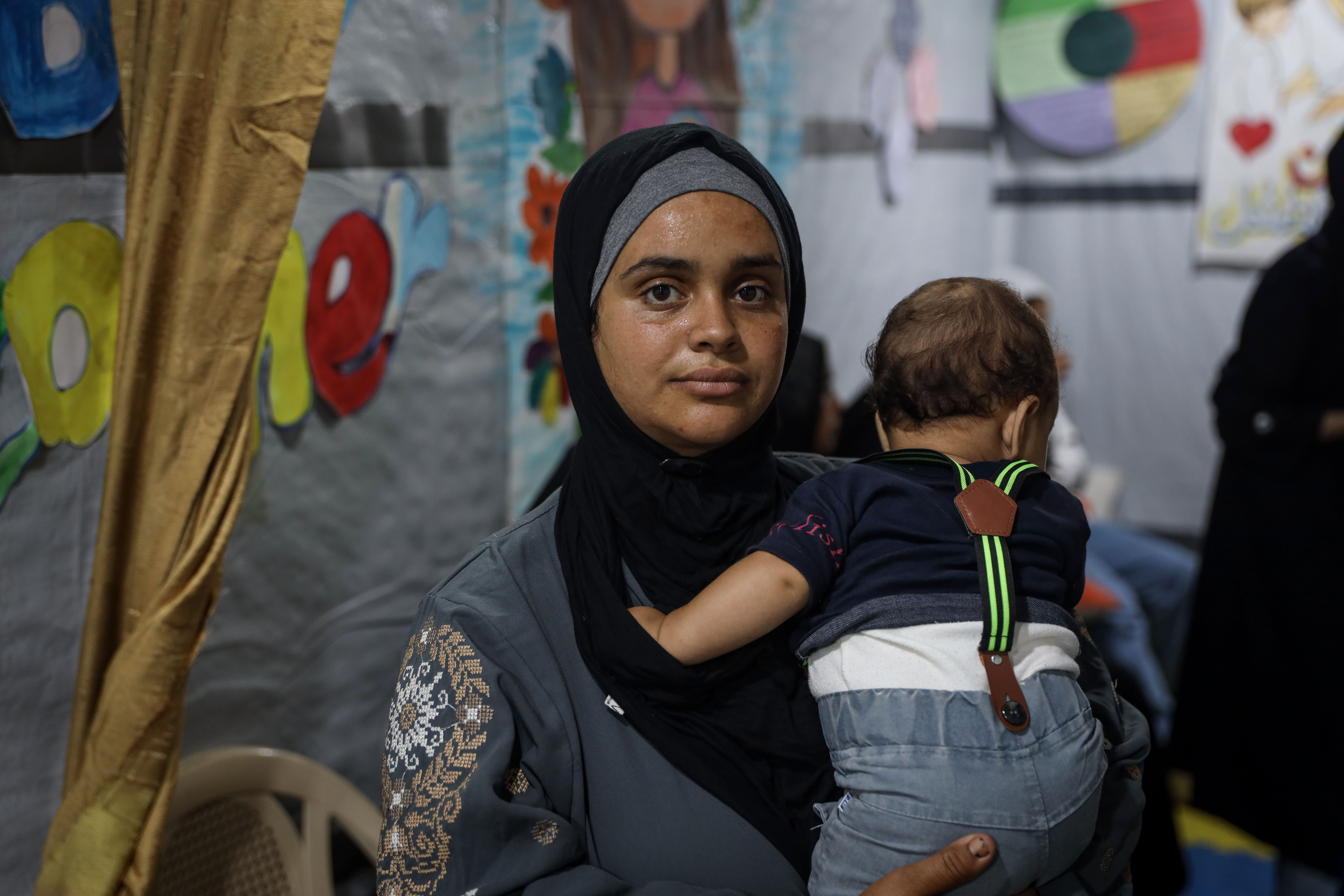 Hiba al-Masri, a displaced mother of four, breastfeeds her three-month-old son while caring for her other children in a crowded tent [Abdelhakim Abu Riash/ Al Jazeera]