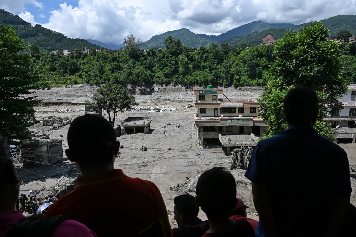 People watch from a rooftop as houses lay deluged in sludge.
