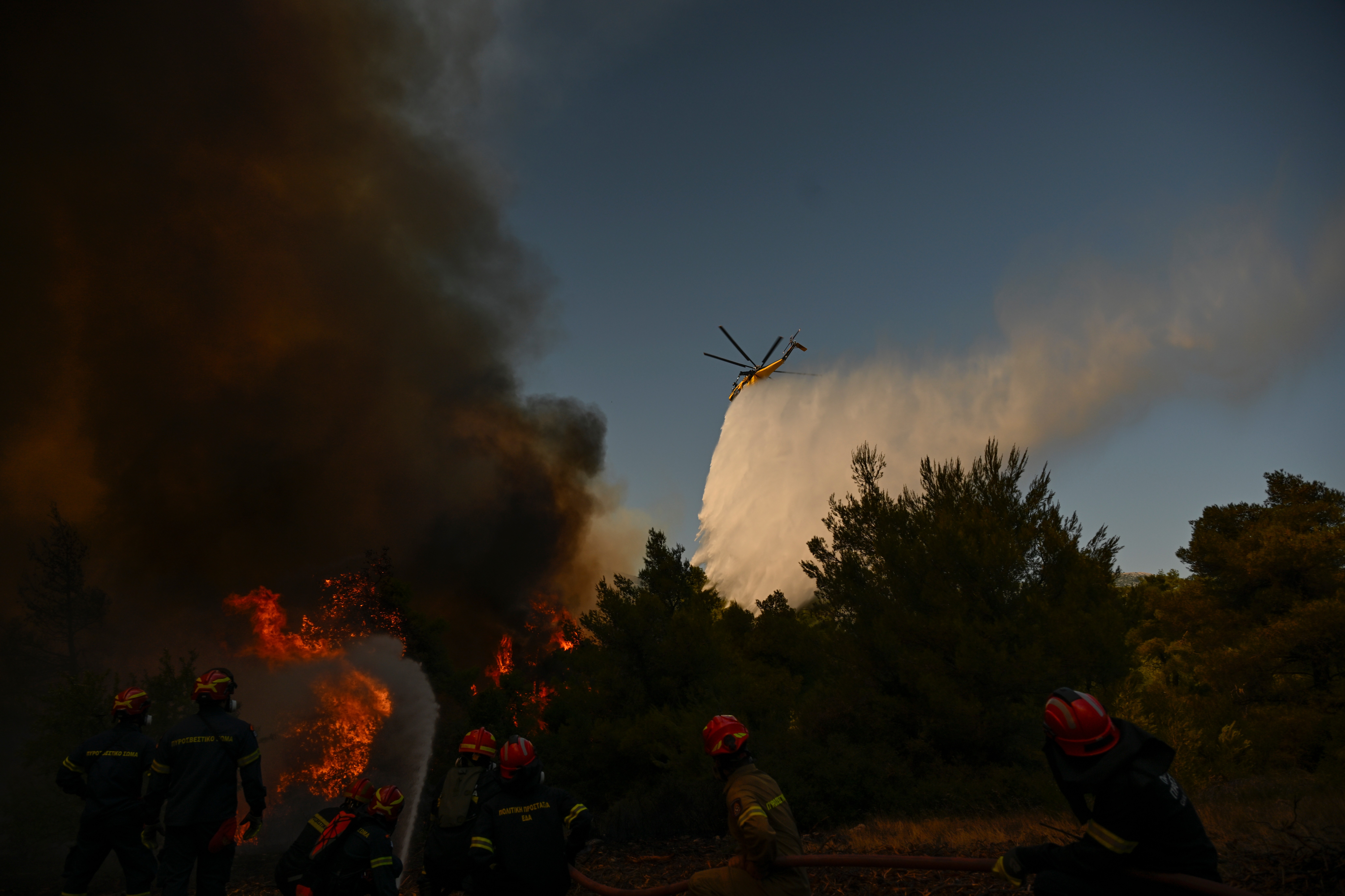 A firefighting helicopter drops water over a smoke-filled forest during a wildfire near Porto Germeno, northwest of Athens, Greece, Sunday, Aug. 2, 2026. (AP Photo/Michael Varaklas)