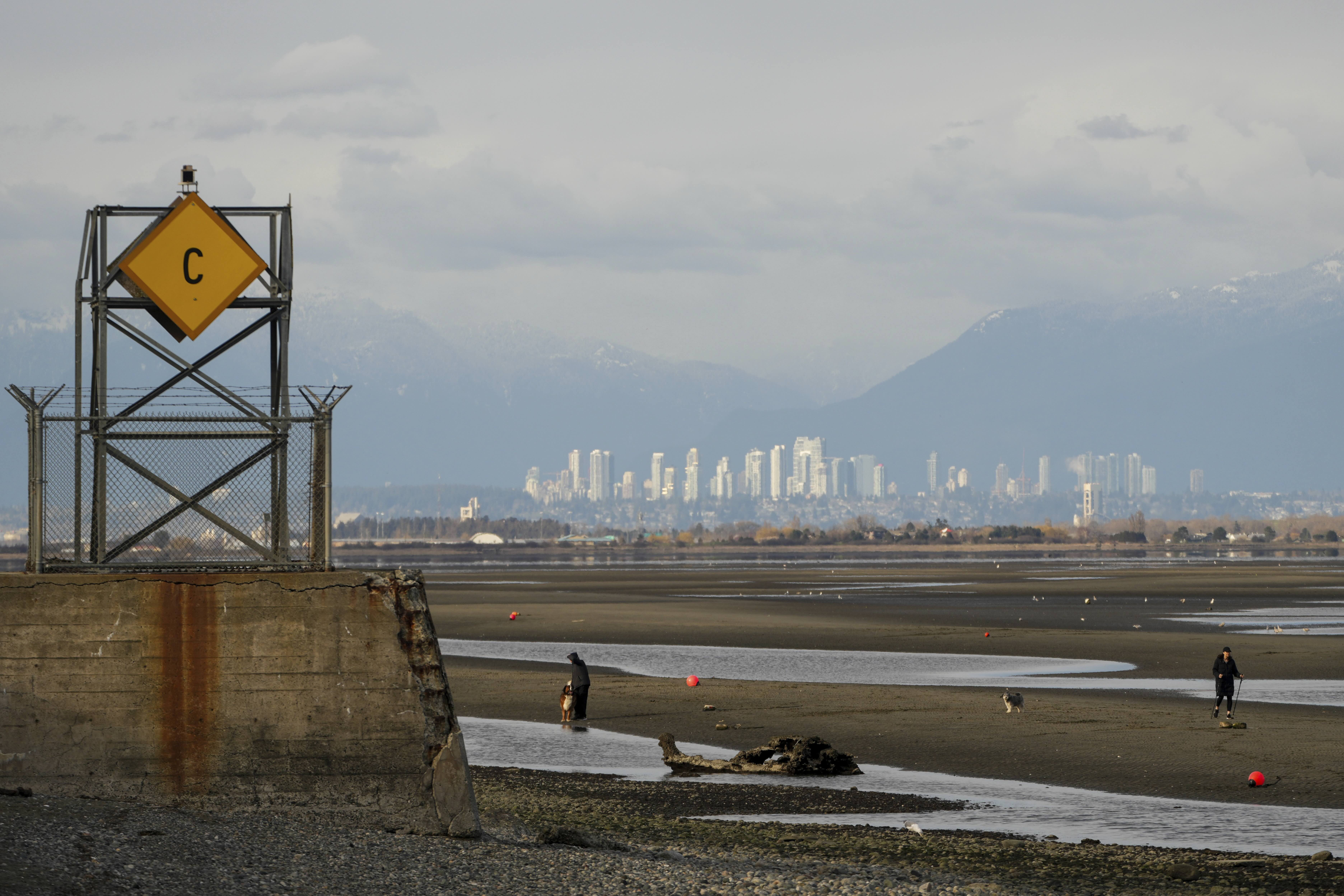 People walk on the Canadian side of Maple Beach during low tide, with the international boundary line marked by a cement tower at left, as seen from Point Roberts, Washington, the United States, on March 18, 2025