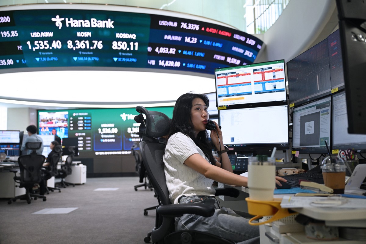 A currency dealer talks on the phone as she monitors exchange rates.