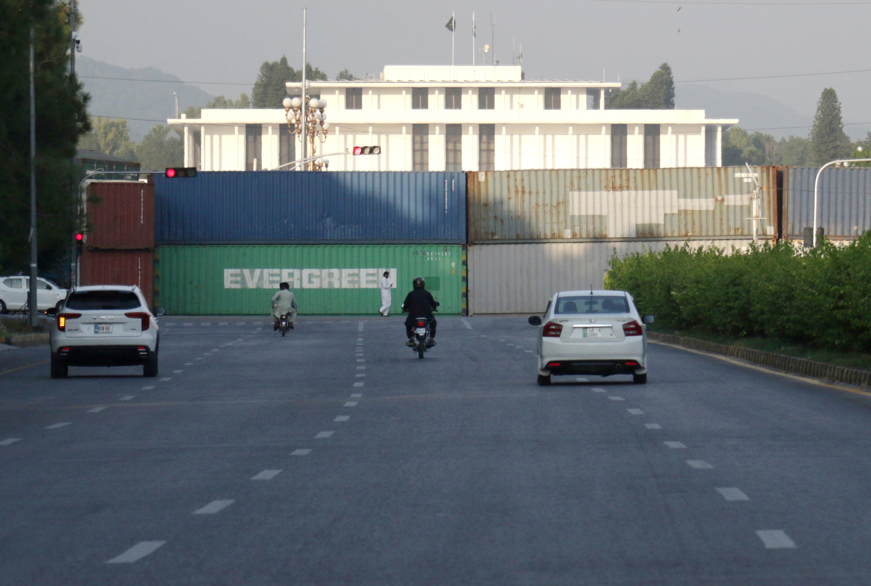 epa13248317 Commuters pass shipping containers lining Islamabads Red Zone, in Islamabad, Pakistan, 18 September 2026. Authorities have deployed containers and additional security personnel at key roads and entry points ahead of planned opposition protests and a Pakistan Tehreek-e-Insaf (PTI) long march scheduled for September 27, with the party demanding the release of former Prime Minister Khan. The security measures have disrupted traffic and raised concerns about restricted road access and the detention of commercial containers. EPA/SOHAIL SHAHZAD