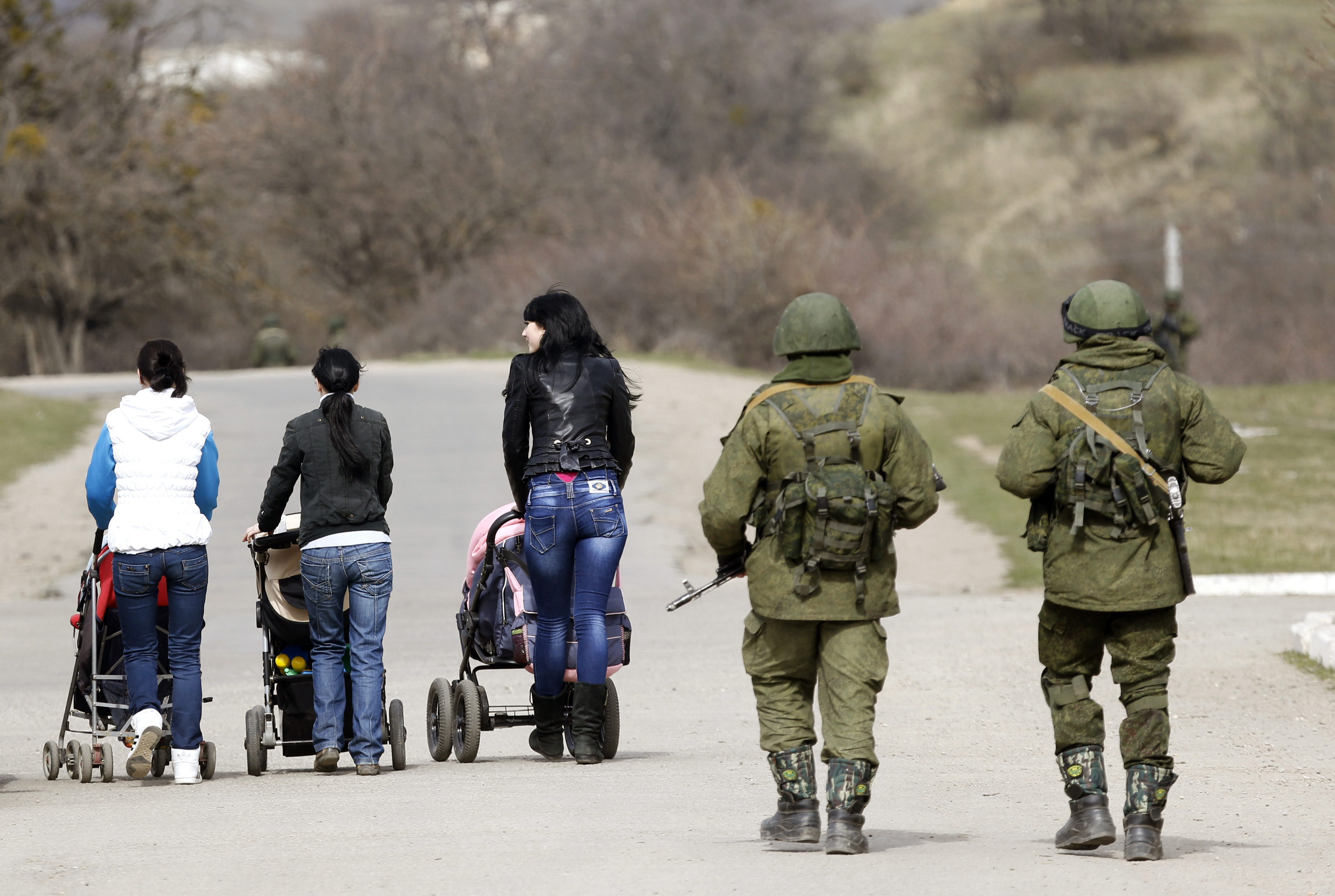 Women with their children in prams walk as armed men, believed to be Russian servicemen, follow them outside an Ukrainian military base in Perevalnoye, near the Crimean city of Simferopol, March 14, 2014. Russia shipped more troops and armour into Crimea on Friday and repeated its threat to invade other parts of Ukraine, showing no sign of listening to Western pleas to back off from the worst confrontation since the Cold War. REUTERS/Vasily Fedosenko (UKRAINE - Tags: POLITICS MILITARY)