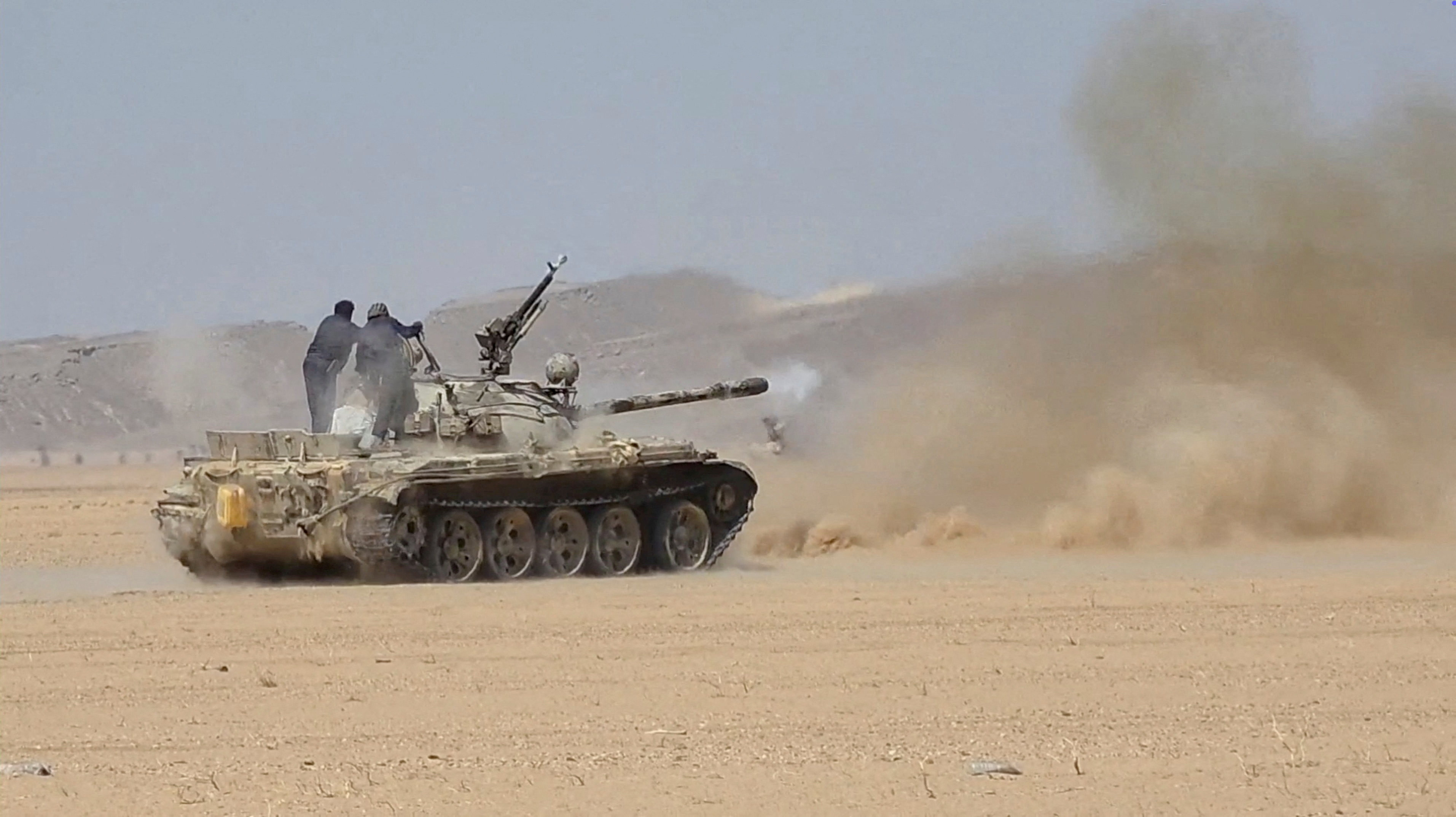 Soldiers fire a tank in desert terrain.
