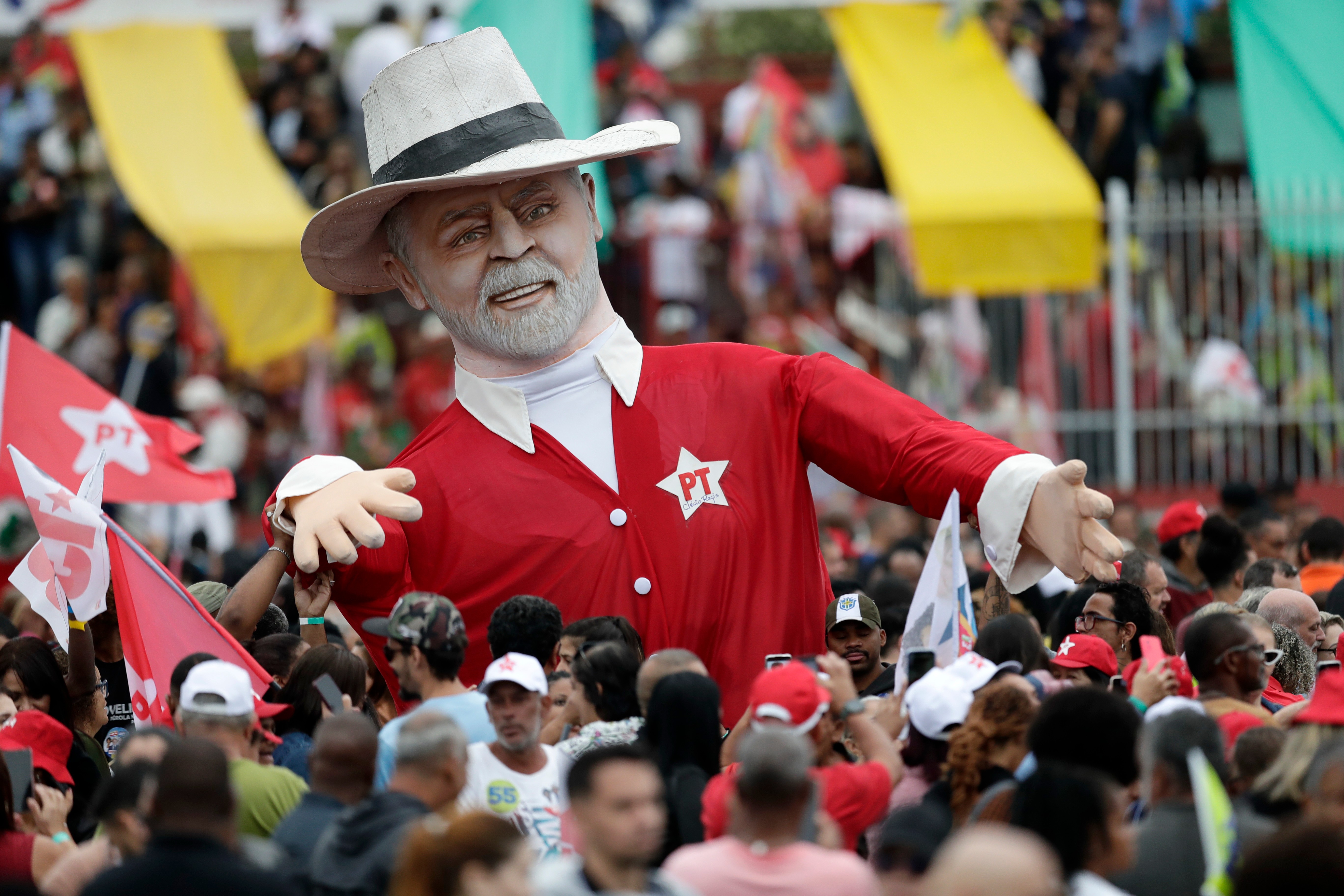 Crowd carrying a large inflatable figure of Lula at an outdoor rally