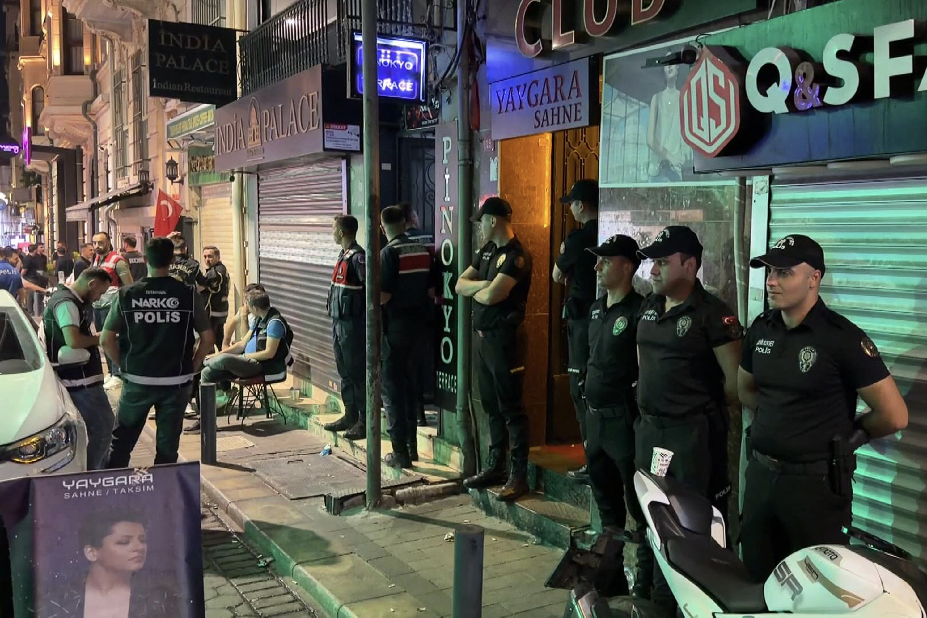Police officers in uniform stand on a pavement outside a building at night.