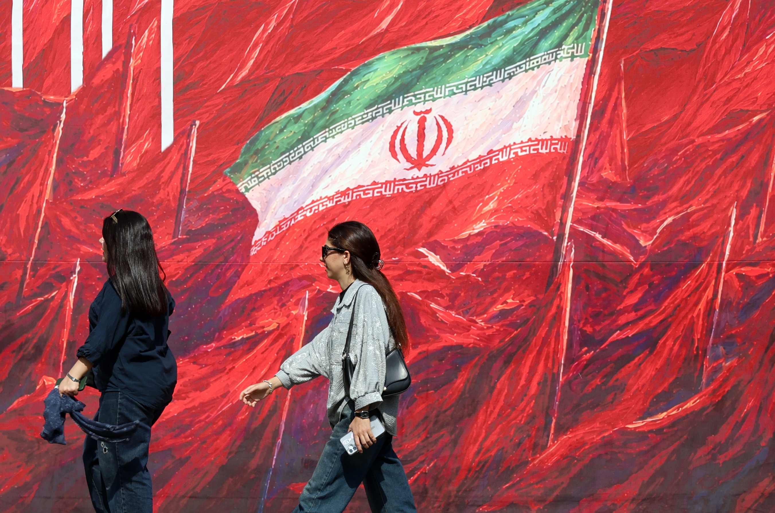 Iranian women walk past a banner featuring Irans national flag in a street in Tehran