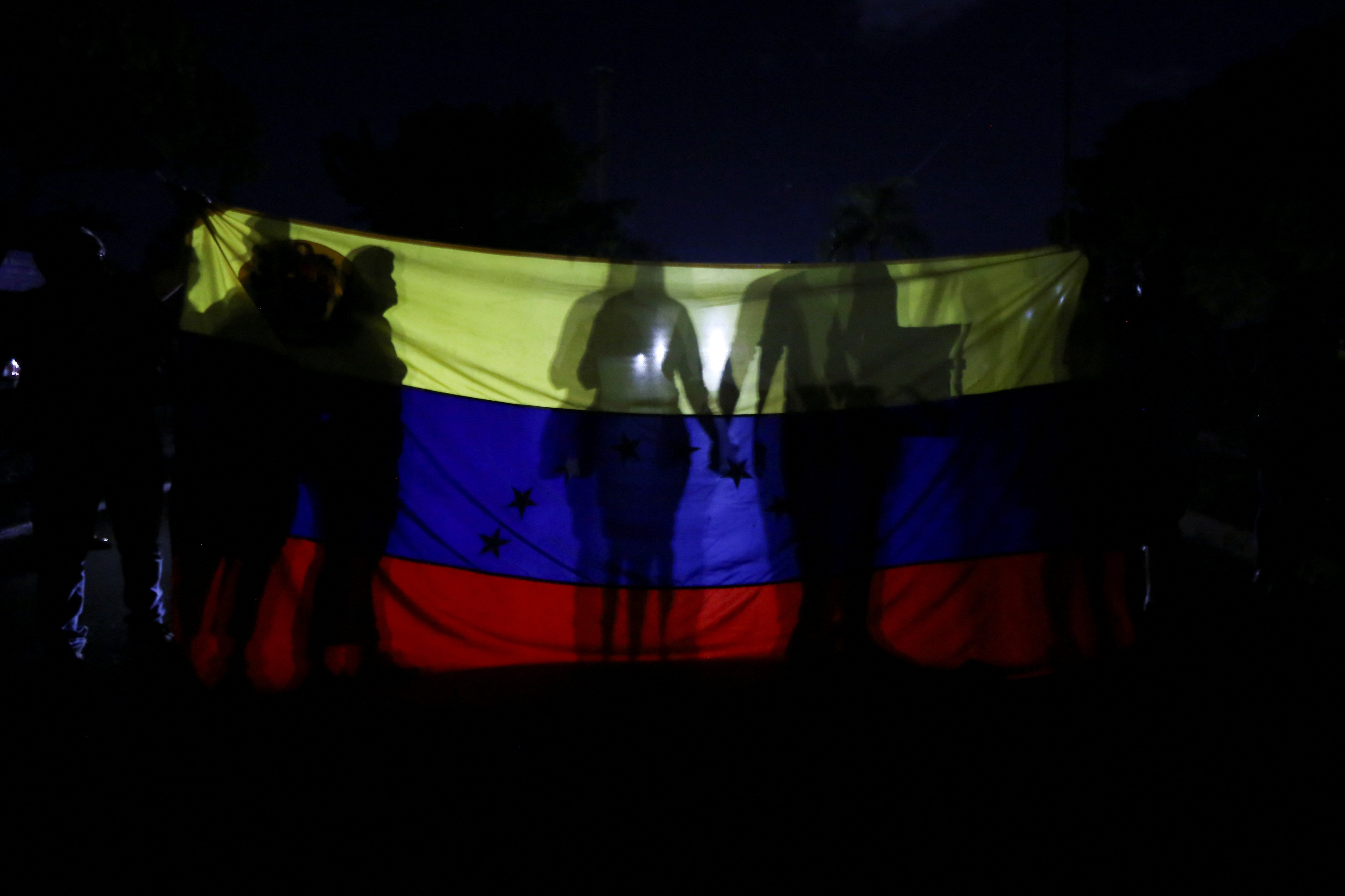 Demonstrators holding hands cast a shadow on a Venezuelan flag held by others during a protest against prolonged power outages in Valencia, Venezuela, October 2, 2026. REUTERS/Juan Carlos Hernandez