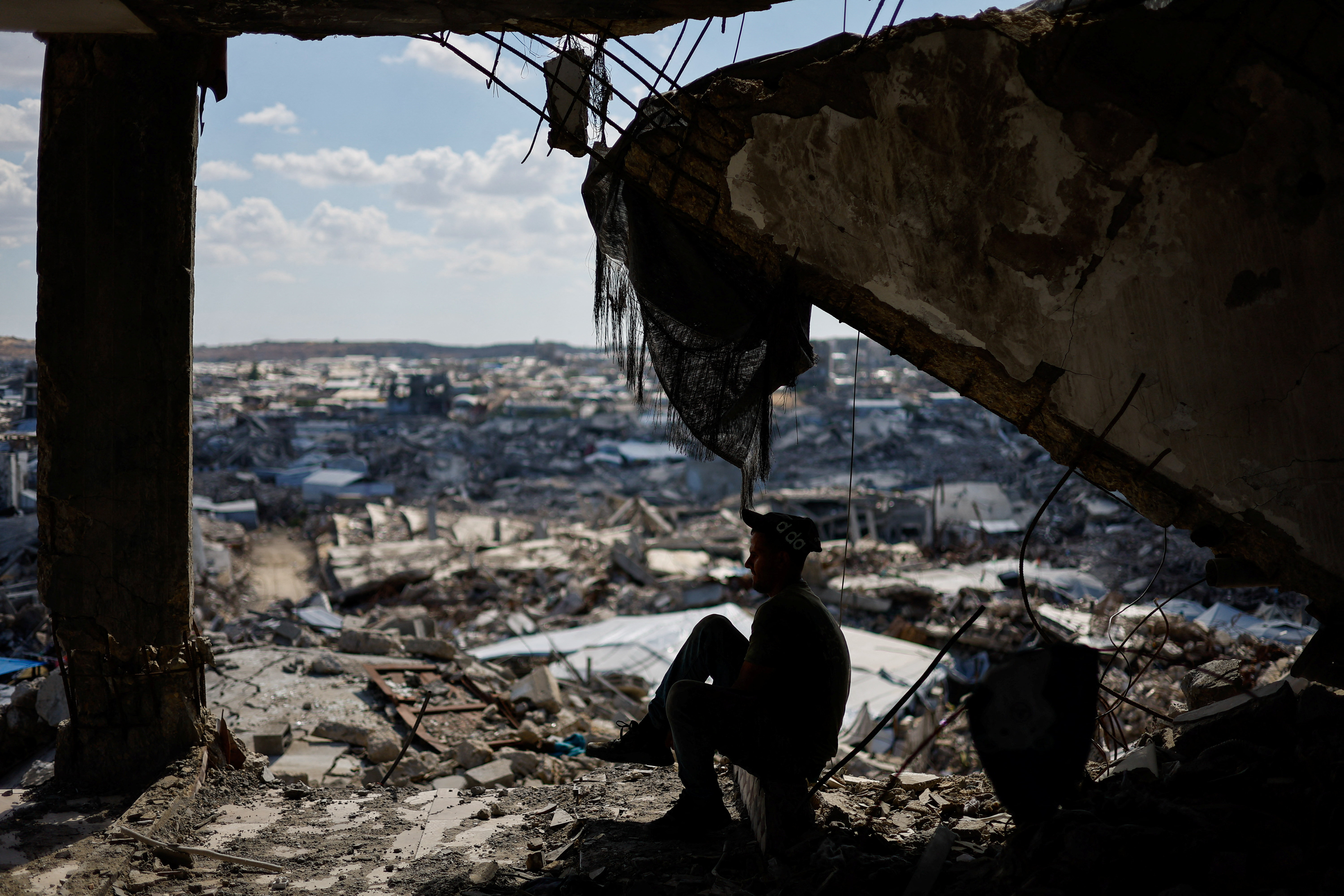 A Palestinian sits in the ruins of a building destroyed during the war, in Gaza City, on October 7, 2026. Mahmoud Issa/Reuters]