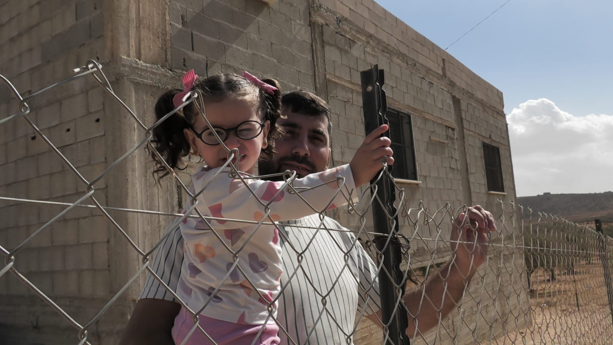 Abd-Al rahman Jaber stands with his daughter near the iron fence he erected around his house to protect it from settlers attacks [Courtesy of Motasem Abu Alia]