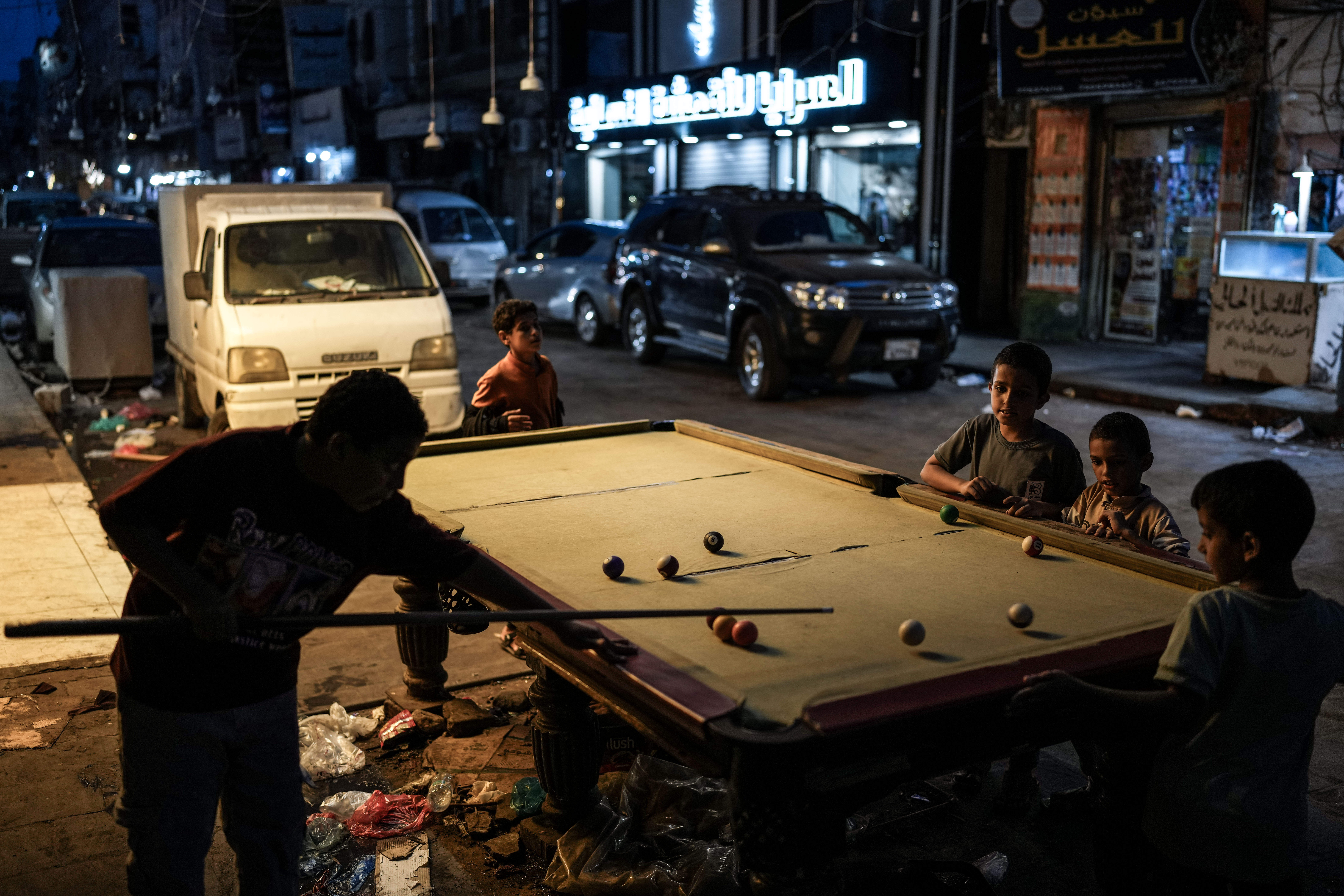Children play billiards on a table set up along a street in Aden at night. For Mohammed, Saeed and Abdullah, the street has become an important space for play and social life when heat and power cuts make staying indoors difficult.