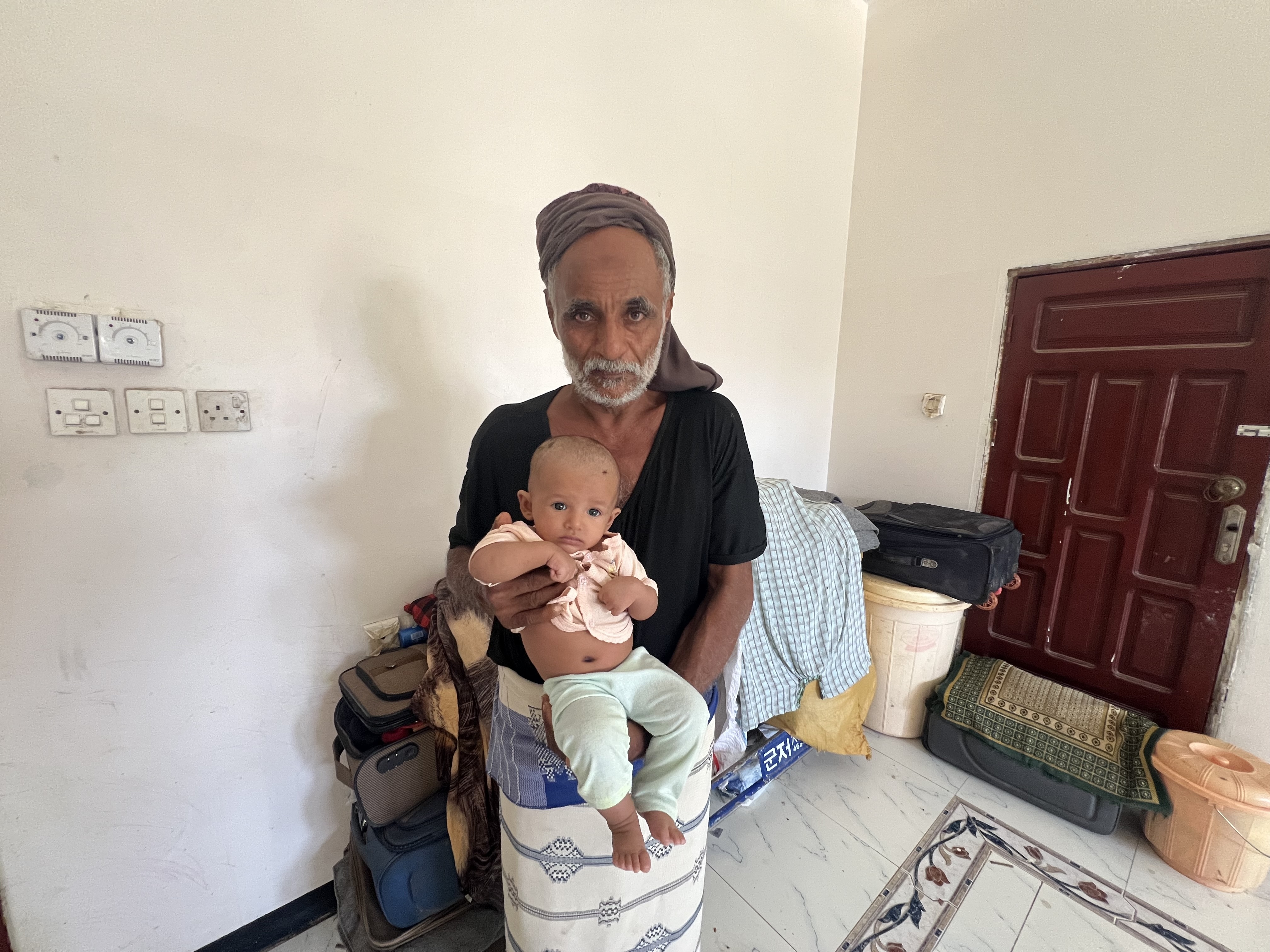 Saeed carries his daughter’s infant, whose father was at sea when the family fled and could not return in time to join them [Do not use - Saeed al-Batati/Al Jazeera]