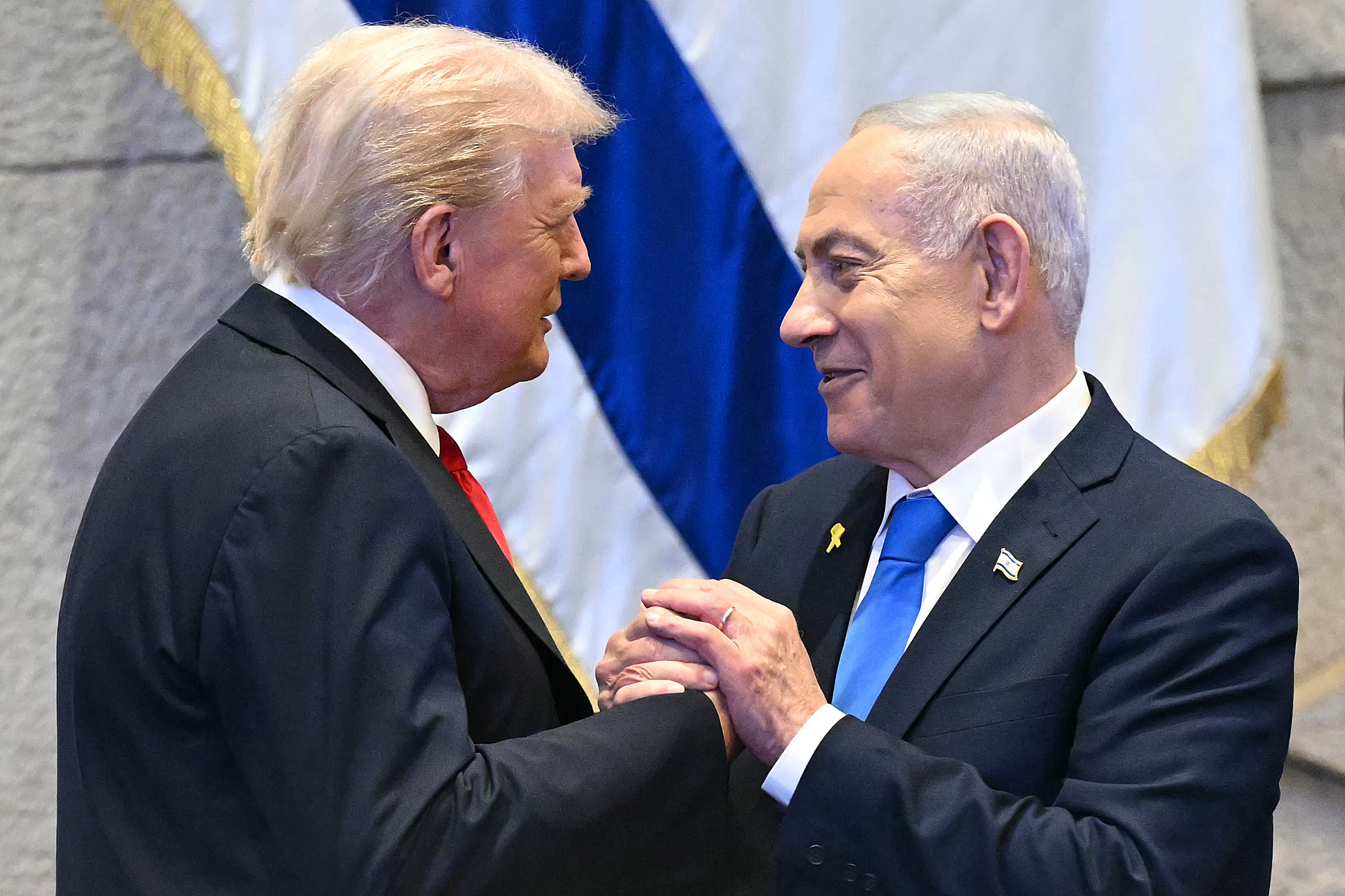 (FILES) US President Donald Trump (L) holds hands and speaks with Israeli Prime Minister Benjamin Netanyahu at the Israeli parliament, the Knesset, in Jerusalem on October 13, 2025.