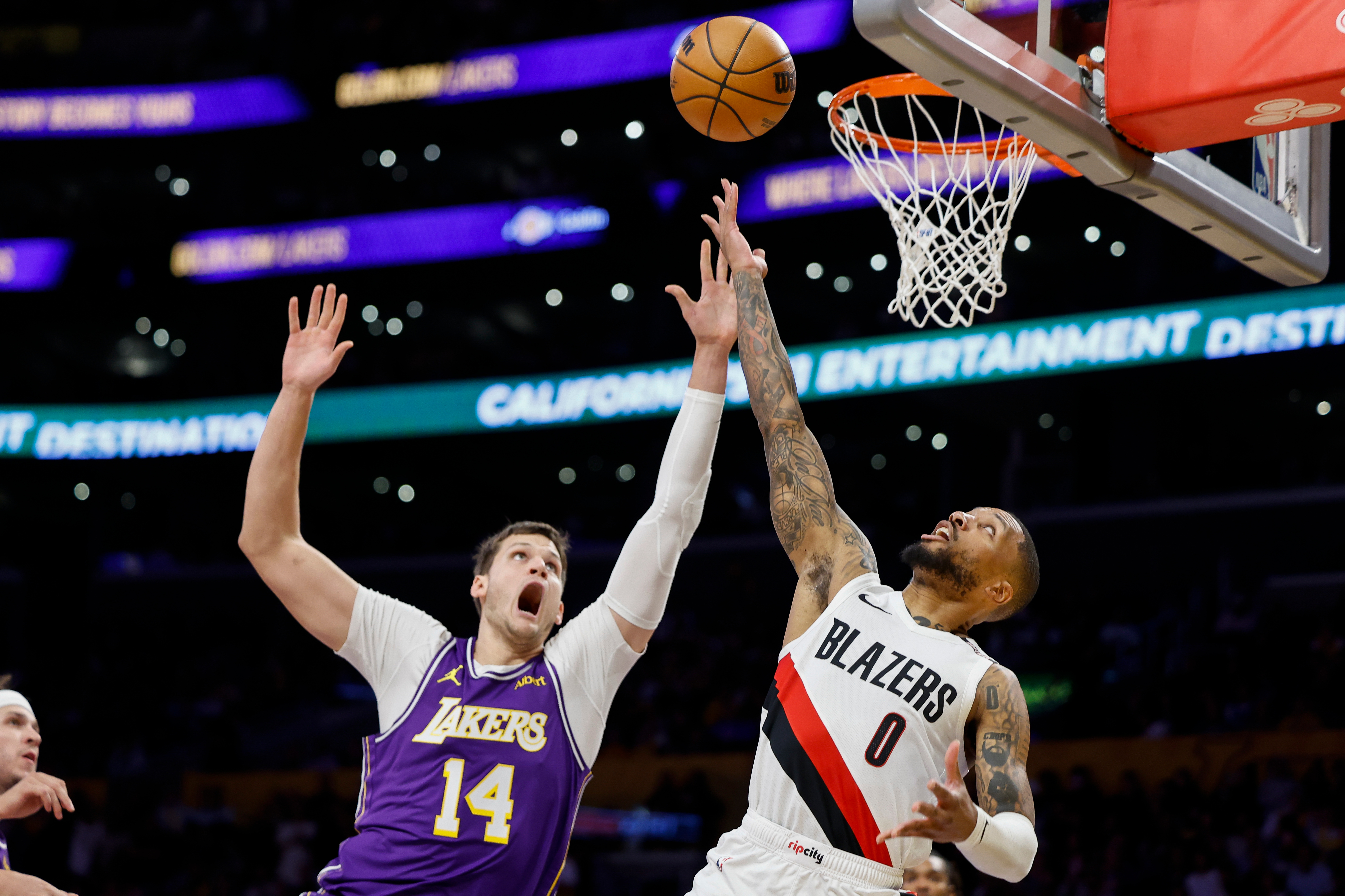 Portland Trail Blazers guard Damian Lillard (0), left, drives to the basket with the ball while being guarded by Los Angeles Lakers center Walker Kessler (14), right.