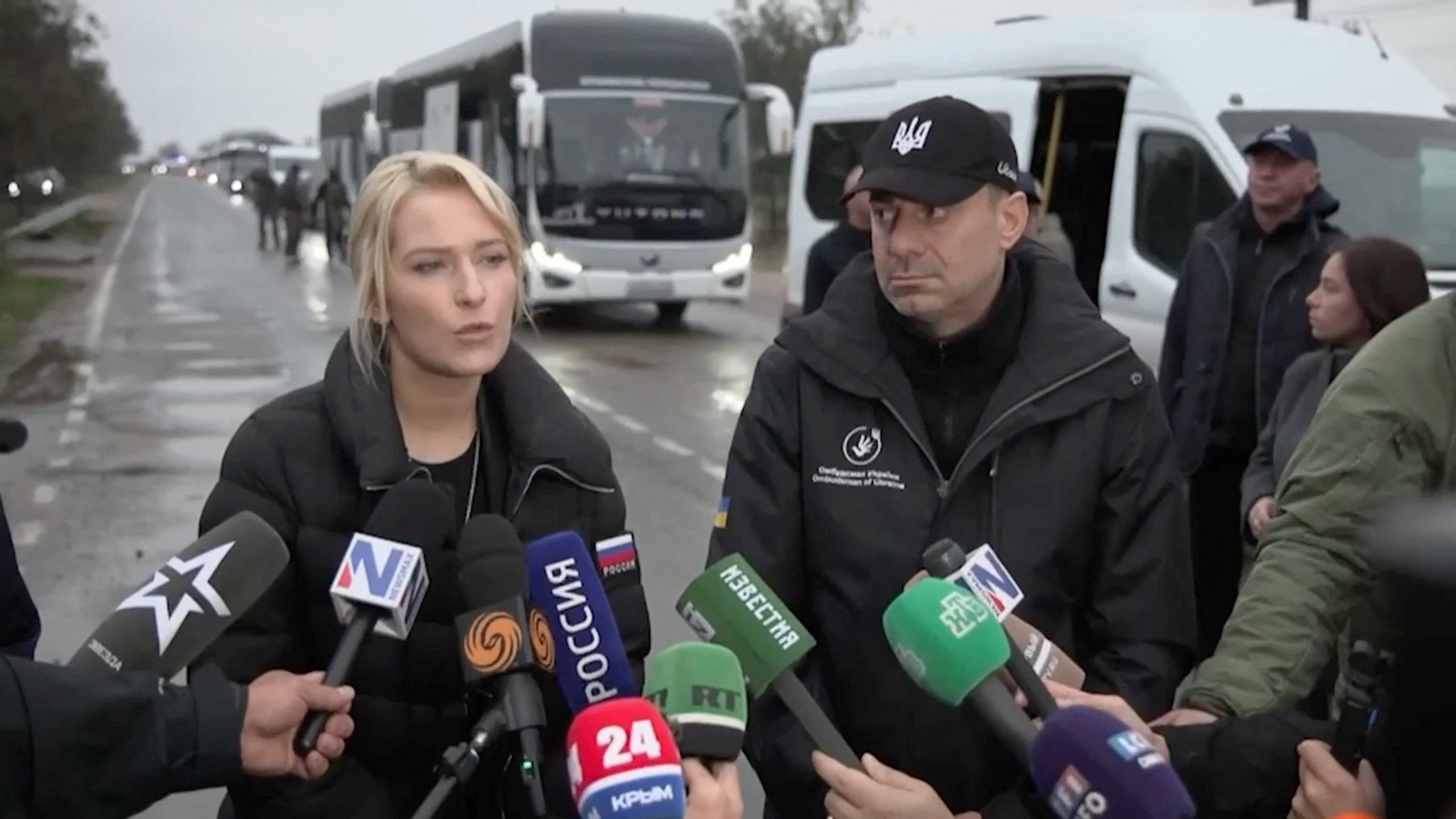 Russia's Human Rights Commissioner Yana Lantratova and Ukraine's Human Rights Ombudsman Dmytro Lubinets speak to the press with buses behind them.